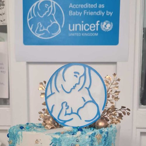 Cake with UNICEF baby friendly logo icing under wall sign for accreditation